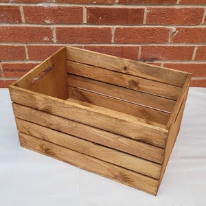 Puede incluir: Una caja de madera grande con un acabado de tinte marr&oacute;n natural. La caja tiene un asa en el lateral y est&aacute; hecha de tablas de madera resistentes.