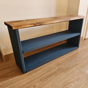May include: A wooden shelf unit with two shelves, painted dark blue. The top shelf is made of natural wood and has a rustic finish.