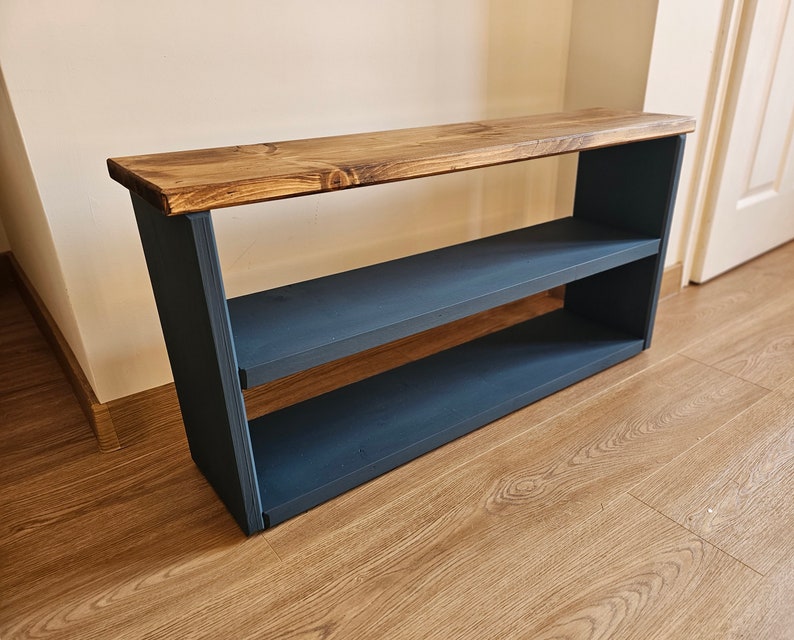 May include: A wooden shelf unit with two shelves, painted dark blue. The top shelf is made of natural wood and has a rustic finish.