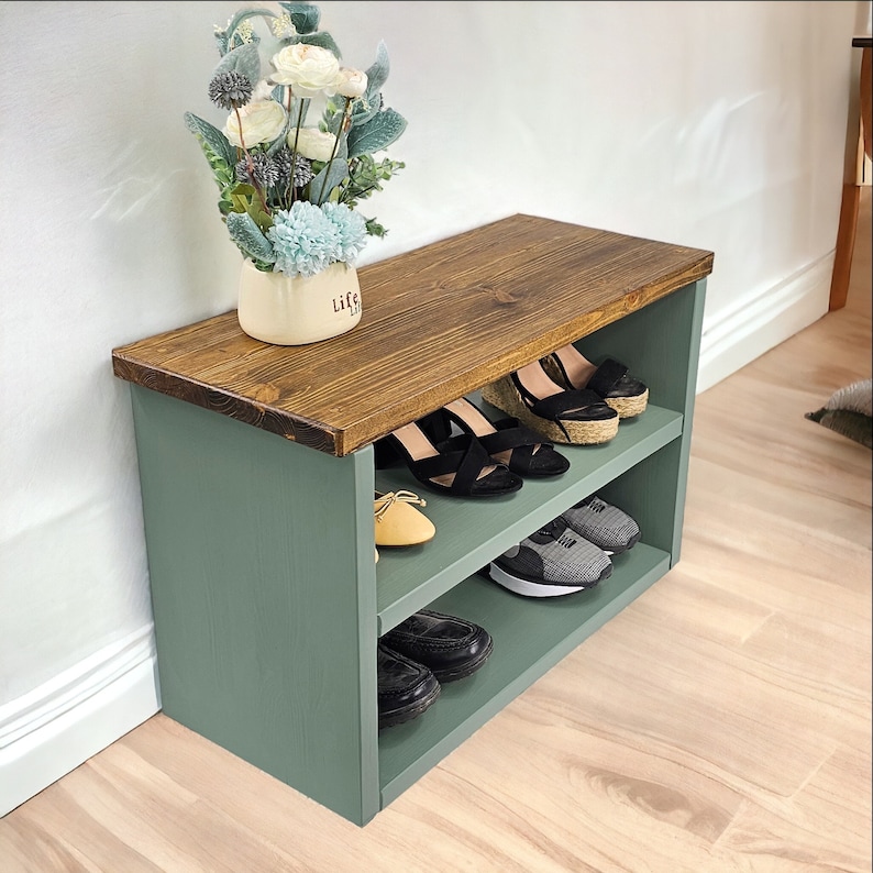 May include: A two-tiered shoe rack with a wooden top and green painted sides. The top shelf is made of wood and the bottom shelf is made of metal. The rack is filled with shoes, including sandals, sneakers, and loafers.