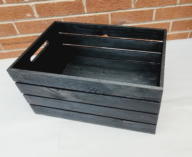 Puede incluir: Una caja de madera negra con un asa en el lateral. La caja tiene cuatro listones en la parte delantera y los laterales.