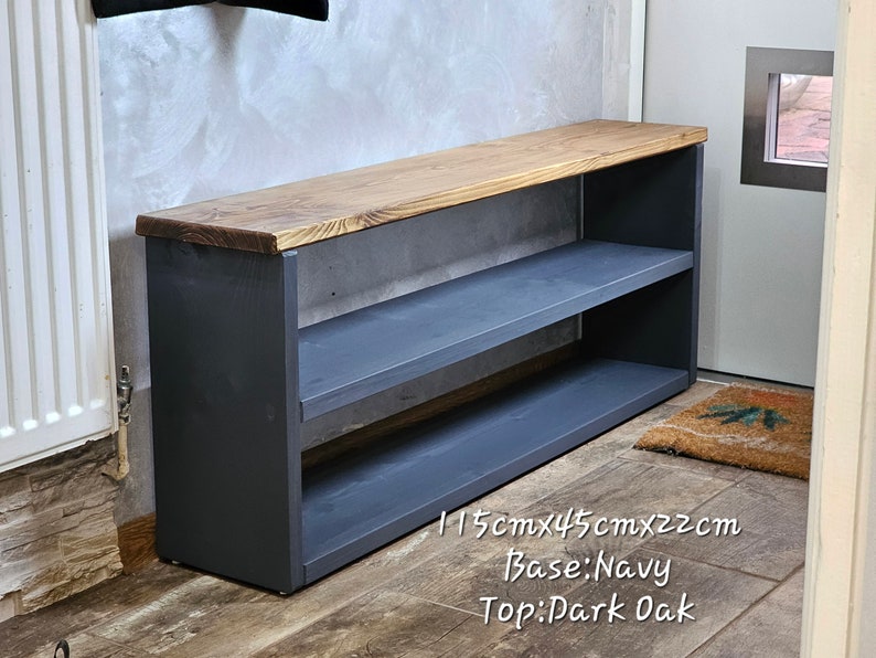 Op de afbeelding: Een schoenenrek met een bovenblad van donker eikenhout en een donkerblauwe basis. Het rek heeft twee planken en meet 115 cm x 45 cm x 22 cm.
