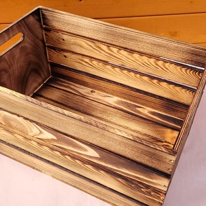 Puede incluir: Una caja de madera r&uacute;stica con una mancha marr&oacute;n oscura y un acabado de madera natural. La caja tiene un asa en el lateral y est&aacute; hecha de tablones de madera.