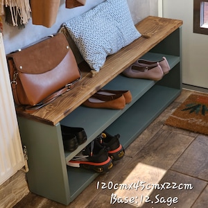 May include: A wooden shoe bench with two shelves, painted sage green with a dark oak top. The bench is 47 inches long, 18 inches wide, and 9 inches tall. It has a cushion on top and is decorated with a brown leather bag, a patterned pillow, and shoes.