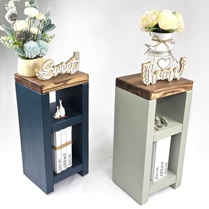 May include: Two wooden side tables, one navy blue and one sage green, each with a dark brown top. The navy table has a "Sweet" sign, while the green table has a "Home" sign. Both have a shelf with decorative items and books.