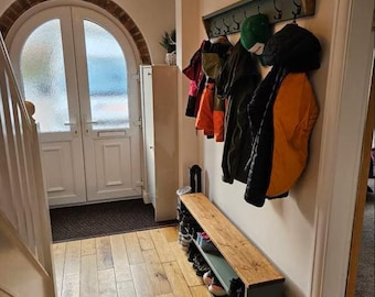 May include: A wooden coat rack with hooks and a shelf, painted in a light green color. The rack is mounted on a wall and has several coats and hats hanging from it. There is a wooden bench with a shelf underneath, also painted in a light green color. The bench is located in a hallway with a wooden floor and a white door.