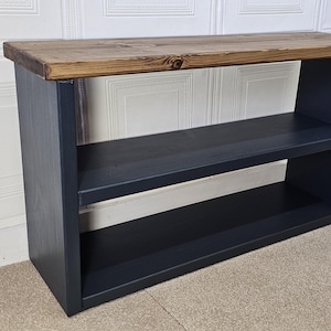 May include: A black wooden shelf unit with two shelves and a rustic wood top. The shelf unit is standing on a beige carpet.