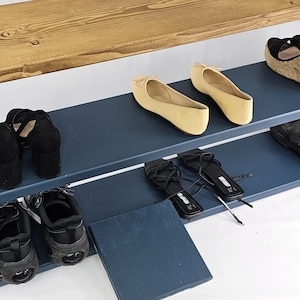 May include: A blue wooden shoe rack with three shelves. The top shelf is made of wood and the bottom two shelves are painted blue. There are shoes on each shelf, including sandals, flats, and heels.