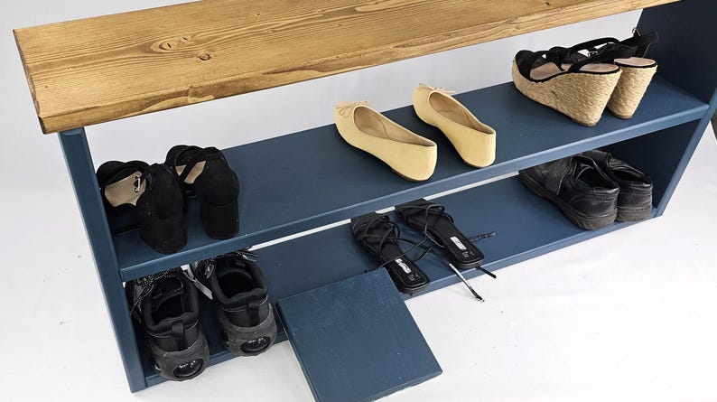 May include: A blue wooden shoe rack with three shelves. The top shelf is made of wood and the bottom two shelves are painted blue. There are shoes on each shelf, including sandals, flats, and heels.