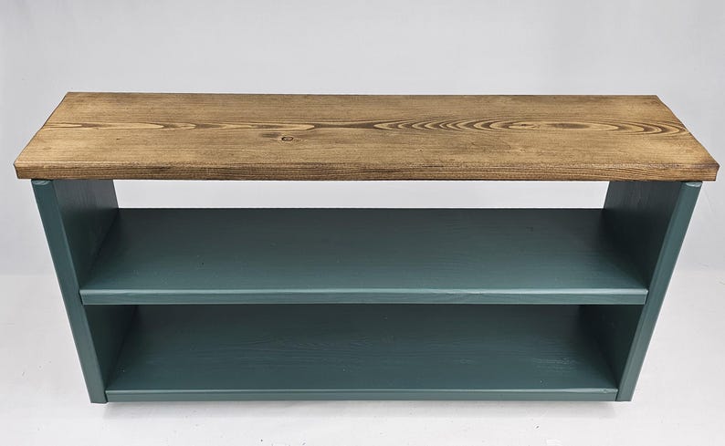 May include: A two-tiered wooden shelf unit with a natural wood top and teal blue painted shelves. The shelf unit is freestanding and has a simple, modern design.