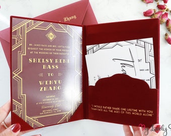 May include: A burgundy velvet wedding invitation box with a gold-embossed art deco design. The box is open, revealing a clear invitation card with the names "Shelsey Rene Bass" and "Wenyu Zhang" printed in gold. The invitation card also includes the date and location of the wedding. The box also includes a white card with the text "Thank you" written in calligraphy.