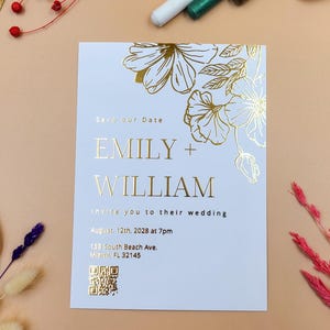 Elegante tarjeta de invitación de boda personalizada con diseño floral dorado en relieve y delicado arte botánico.