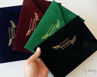May include: Four velvet envelopes in navy blue, burgundy, green, and black with gold lettering that reads "ROLDAN" and a gold floral design.