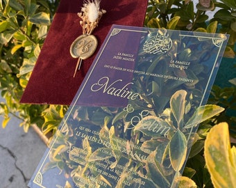 Puede incluir: Una invitación de boda de acrílico transparente con letras doradas. La invitación anuncia el matrimonio de Nadine y Selim, que se celebrará el sábado 13 de febrero de 2021 a las 14:00. La invitación también incluye la dirección de la recepción.