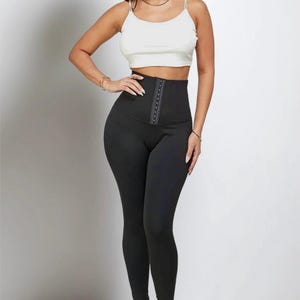 May include: Black high-waisted leggings with a hook-and-eye closure and a white crop top. The leggings are form-fitting and made of a smooth, opaque material. The crop top has thin straps.