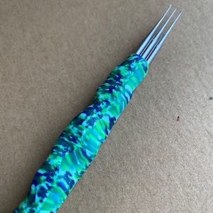 Puede incluir: Primer plano de una herramienta multi-aguja con un mango de camuflaje verde, azul y blanco.