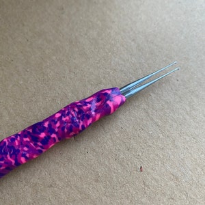 Puede incluir: Un gancho de ganchillo de color rosa y morado con una aguja de doble punta.