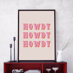 May include: A red shelf unit with black trim and three shelves. The top shelf has a framed print with the text "Howdy" repeated three times in pink letters. The middle shelf has a toy car, a clock, and books. The bottom shelf has more books and two small white cups.