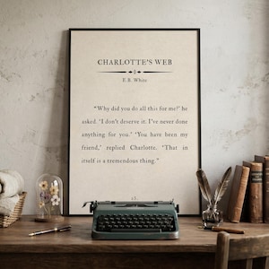 May include: A framed print of "Charlotte's Web" by E.B. White, with a quote from the book. A vintage teal typewriter sits on a wooden desk, along with books, a pen, and a glass cloche with dried flowers.