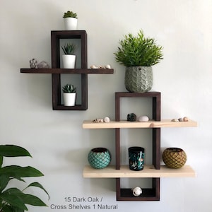 May include: A set of wooden wall shelves in a dark oak finish with one shelf in a natural wood finish. The shelves are arranged in a cross shape and feature decorative items, plants, and small pots. The shelves are labeled "15 Dark Oak / Cross Shelves 1 Natural".