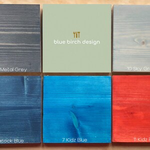May include: Ten wood samples stained in different colors, including ebony black, gun metal gray, sky gray blue, whitewash, kidz green, peacock blue, kidz blue, kidz red, and natural. The text "YIT blue birch design" is printed on a light green sample.