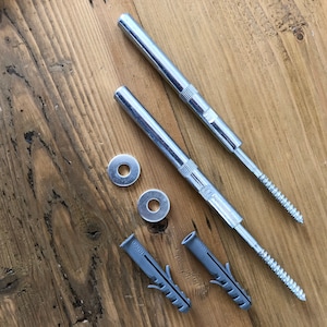 May include: Two silver metal screws with a threaded end and a flat head, two silver metal washers, and two gray plastic anchors. The screws and anchors are on a wooden surface.