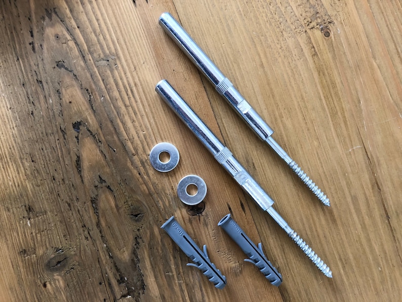 May include: Two silver metal screws with a threaded end and a flat head, two silver metal washers, and two gray plastic anchors. The screws and anchors are on a wooden surface.
