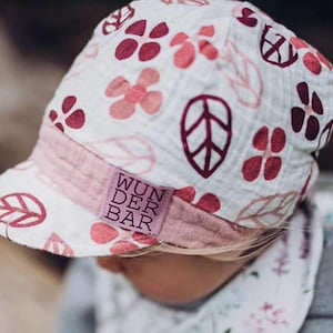 May include: A white and pink patterned baby hat with a brim. The hat features a floral and leaf design in shades of pink and burgundy. The brim is a solid pink color with the text "WUNDER BAR" on a small label.