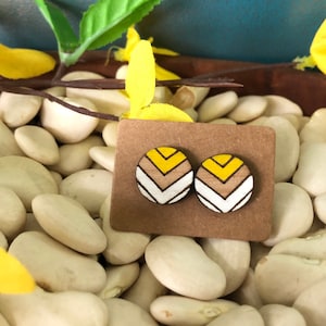 May include: A pair of wooden earrings with a geometric pattern in yellow, white, and brown. The earrings are displayed on a brown card.