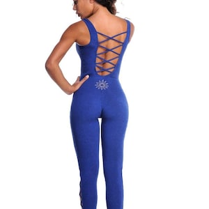 May include: A royal blue jumpsuit with a crisscross back design and a sunburst emblem. The sleeveless one-piece garment features a fitted silhouette and stirrup-style bottoms. The back of the jumpsuit has a crisscross design.