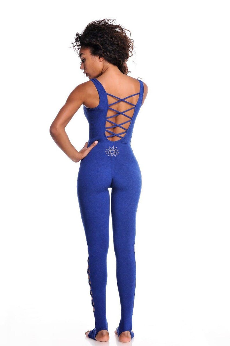 May include: A royal blue jumpsuit with a crisscross back design and a sunburst emblem. The sleeveless one-piece garment features a fitted silhouette and stirrup-style bottoms. The back of the jumpsuit has a crisscross design.