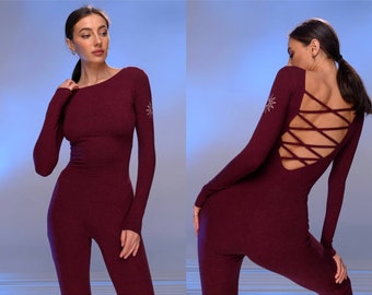 Könnte beinhalten: Burgunderfarbener Jumpsuit mit langen Ärmeln und einem Rundhalsausschnitt. Der Rücken hat ein Kreuz-und-Quer-Design. Ein kleines, gesticktes Sternmotiv befindet sich auf dem linken Ärmel. Der Jumpsuit ist figurbetont und aus Rippstrick gefertigt.