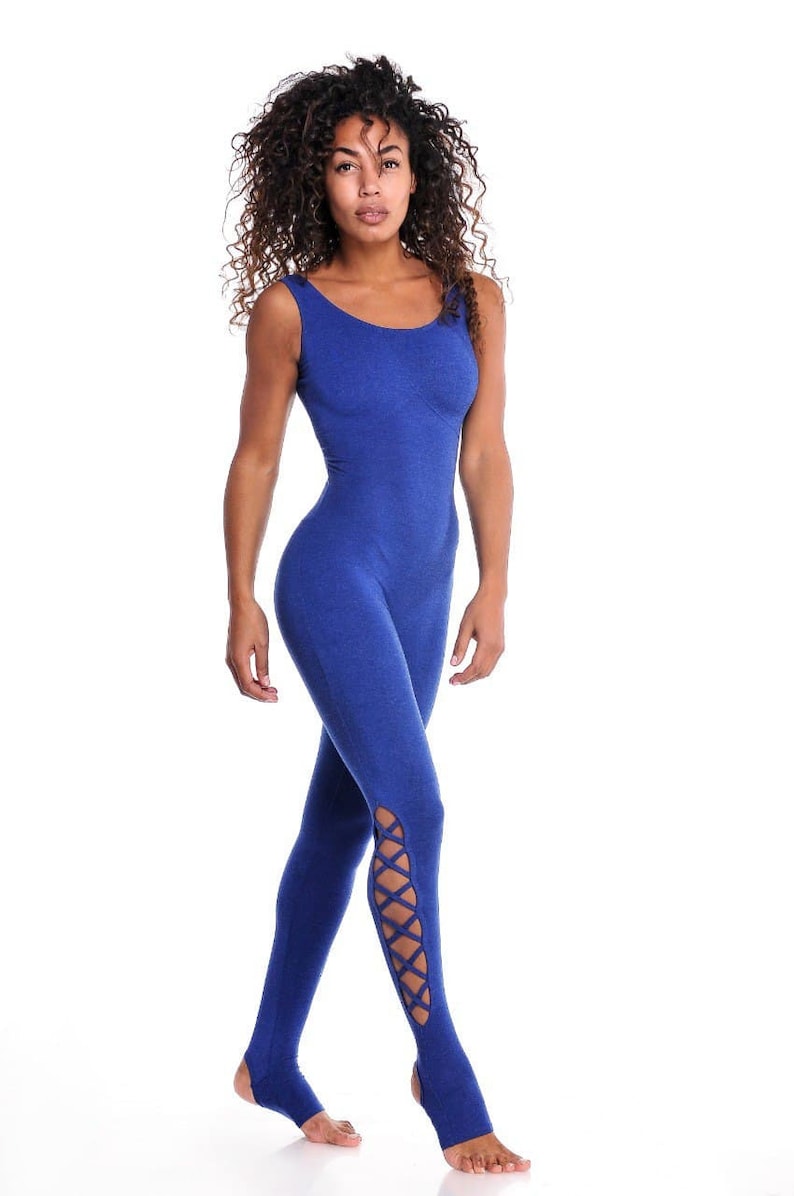 May include: A blue jumpsuit with a scoop neckline and stirrup bottoms. The jumpsuit has crisscross detailing on the lower legs. The model is standing against a white background.