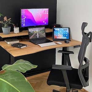 Pode incluir: Uma mesa de pé preta e madeira com uma cadeira preta, um laptop, um tablet, um monitor e uma planta em vaso. A mesa tem uma prateleira acima da mesa.