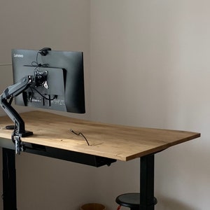 Może przedstawiać: Czarny monitor z logo Lenovo jest zamontowany na czarnym ramieniu wystającym z drewnianego biurka. Biurko ma czarną szufladę i czarne nogi. Biurko jest podniesione na czarnym stojaku.