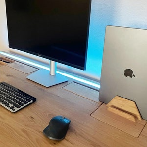 May include: A wooden desk with a monitor, keyboard, and mouse. A silver laptop is in a wooden stand. The desk has built-in compartments and a blue LED light strip.