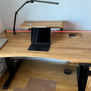 Könnte beinhalten: Ein Stehpult aus Holz mit einem schwarzen Gestell und einem roten LED-Lichtstreifen, der entlang der hinteren Kante verläuft. Ein Laptop und ein Tablet befinden sich auf dem Schreibtisch, und über dem Schreibtisch befindet sich ein kleines Regal.