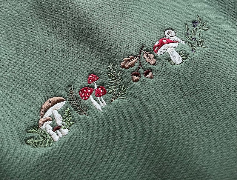 May include: Green fabric with embroidered mushrooms and leaves in shades of brown, red, and white.