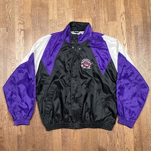 May include: Vintage Raptors jacket in black, purple, and white. The jacket has a snap-front closure, a stand-up collar, and the Raptors logo on the chest. The sleeves and shoulders are purple, with white and black panels.