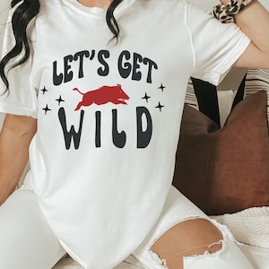 May include: White t-shirt with a red running wild boar graphic and the text "Let's Get Wild" in black.