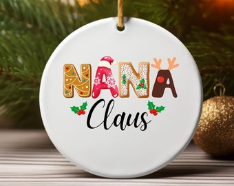 May include: White ceramic Christmas ornament with the text "NANA Claus" in gingerbread-style letters with red, green, and white frosting. The letters are decorated with sprinkles and a red and white Santa hat.