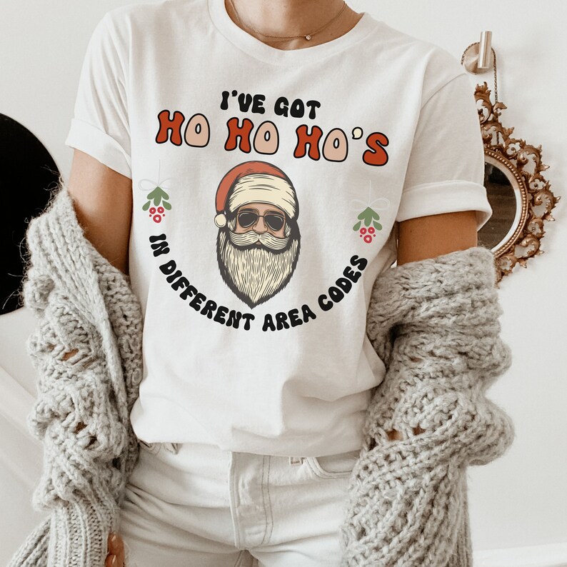 May include: White t-shirt with a Santa Claus graphic and the text "I've got Ho Ho Ho's in different area codes".