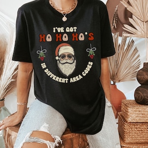 May include: Black t-shirt with a Santa Claus graphic and the text "I've got Ho Ho Ho's in different area codes".