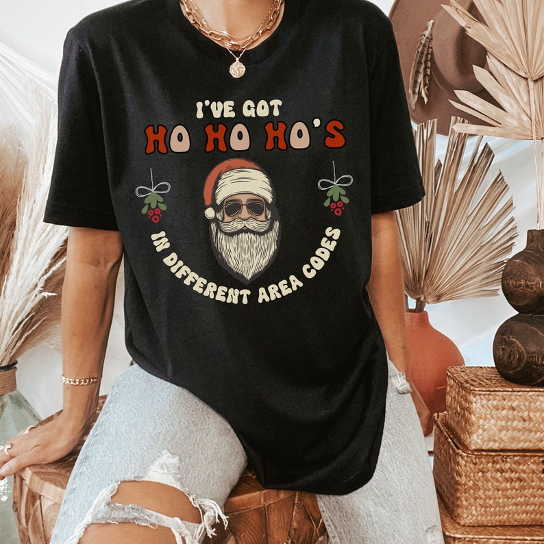 May include: Black t-shirt with a Santa Claus graphic and the text "I've got Ho Ho Ho's in different area codes".