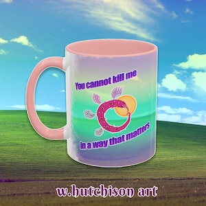 May include: White ceramic mug with a pink handle and interior. The mug features a colorful design with the text "You cannot kill me in a way that matters" and a stylized creature illustration. The artist's name, "w.hutchison art", is at the bottom.