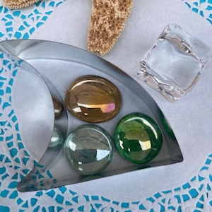 May include: A silver metal cookie cutter shaped like a shark fin with five iridescent glass stones inside. The cookie cutter is on a white doily with a blue background.