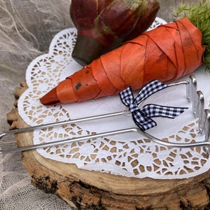 May include: A silver metal carrot-shaped tool with a black and white checkered bow. The tool is on a white doily on a wooden surface.