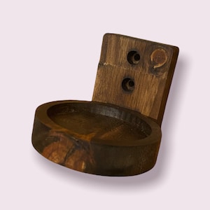 Pu&ograve; includere: Un supporto a parete in legno marrone scuro con un ripiano circolare. Il ripiano ha un bordo liscio e arrotondato e una finitura leggermente pi&ugrave; scura rispetto al supporto a parete.