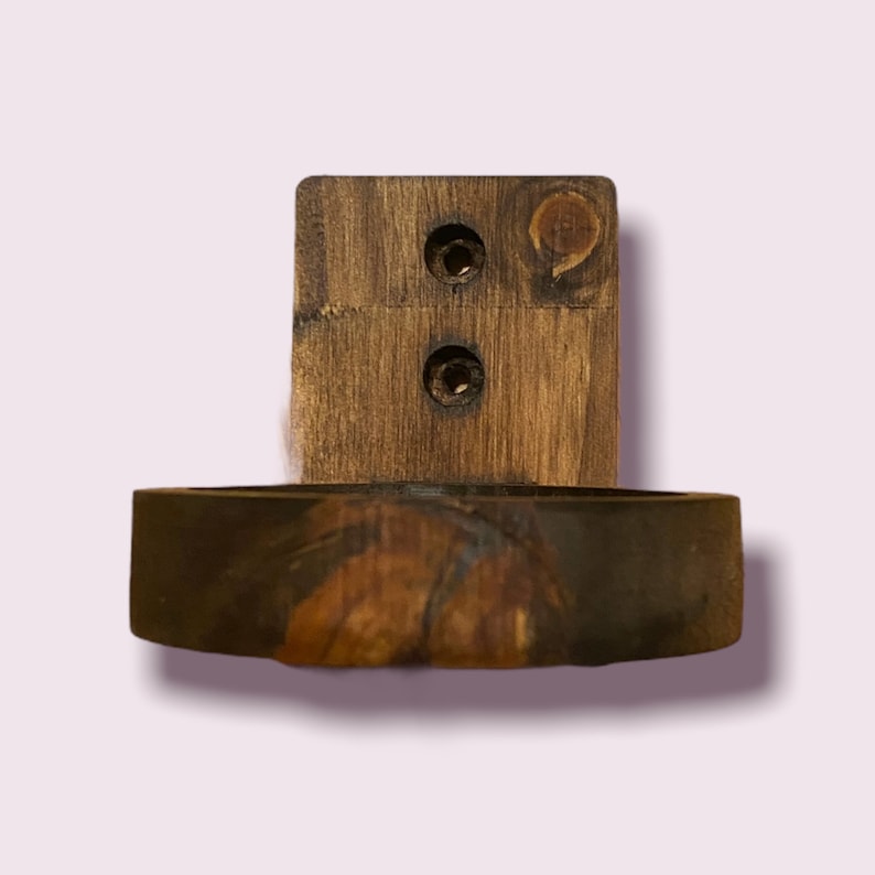 Pu&ograve; includere: Un supporto a parete in legno con due fori per viti e un piatto rotondo in resina fissato sul fondo. Il piatto ha un motivo a marmo marrone, arancione e nero.