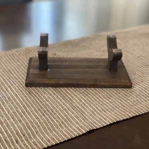 May include: A wooden stand with two upright arms for holding a sword or other long object. The stand is dark brown and has a smooth finish.